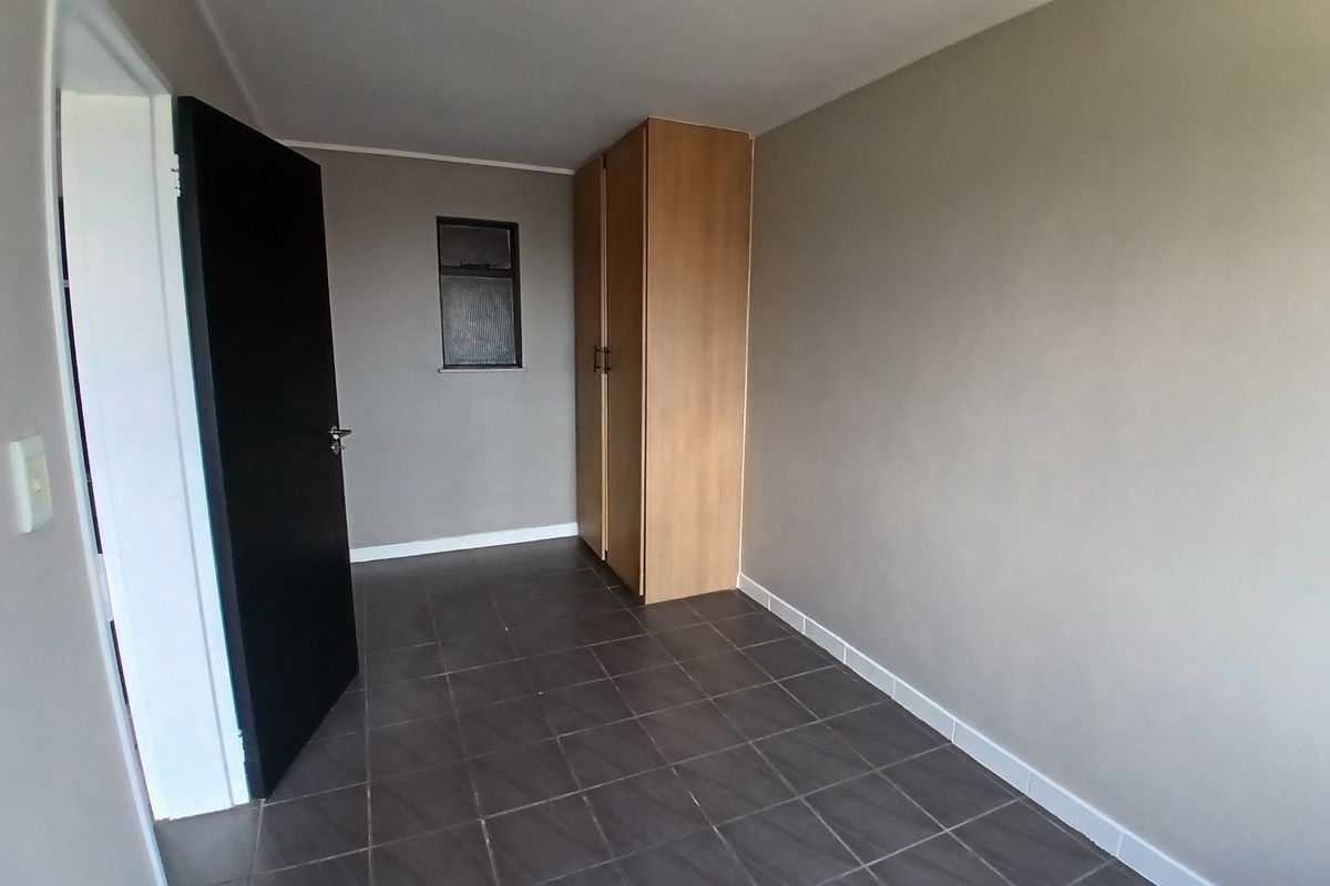 A clean, empty bedroom featuring neutral wall tones, dark tiled flooring, and a built-in wooden wardrobe.
