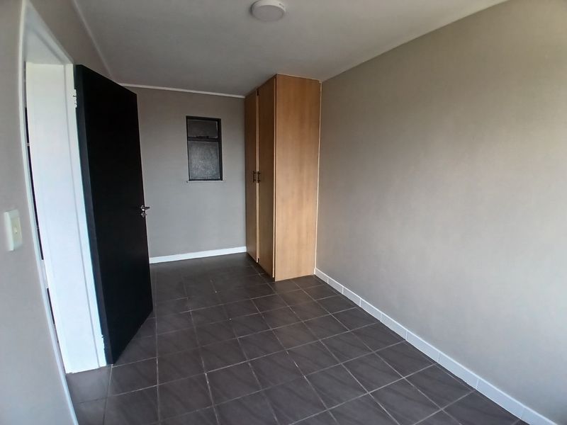 A clean, empty bedroom featuring neutral wall tones, dark tiled flooring, and a built-in wooden wardrobe.