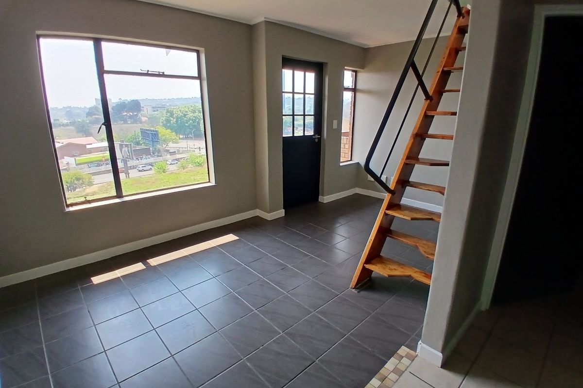 An open-plan living area featuring dark tiled flooring, a timber staircase with a metal handrail, and large windows providing natural light and exterior views.