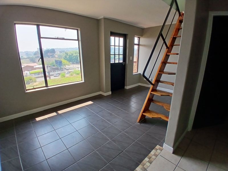 An open-plan living area featuring dark tiled flooring, a timber staircase with a metal handrail, and large windows providing natural light and exterior views.