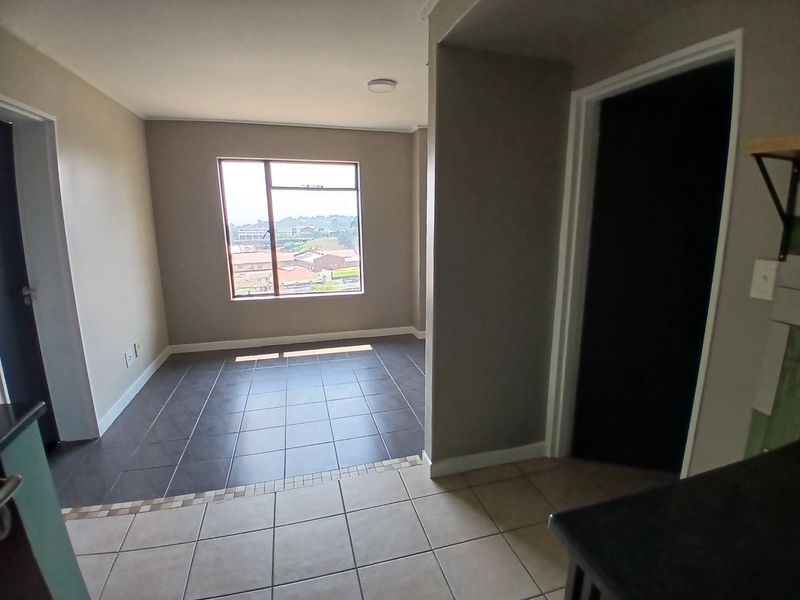An open-plan living area featuring neutral wall tones, tiled flooring throughout, and a large window providing natural light and neighborhood views.