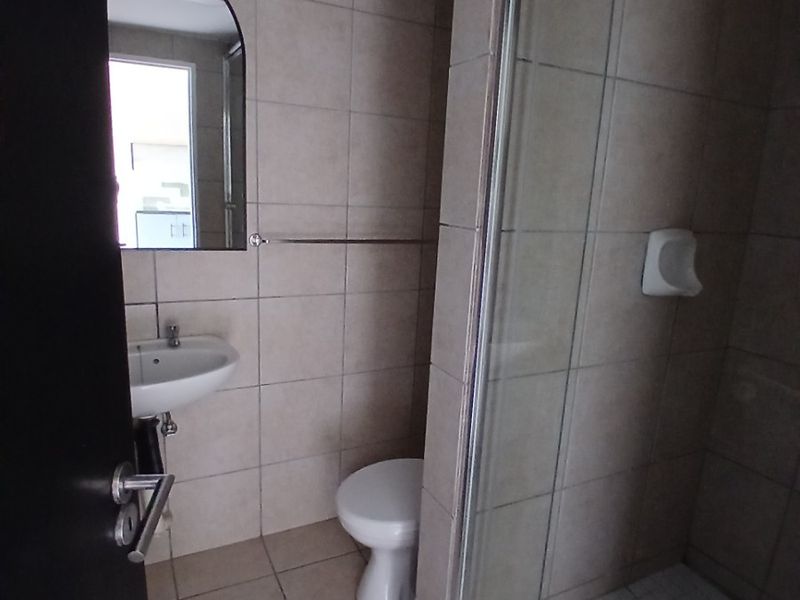 A functional bathroom featuring a glass-enclosed shower, wall-mounted basin, toilet, and neutral floor-to-ceiling tiling.