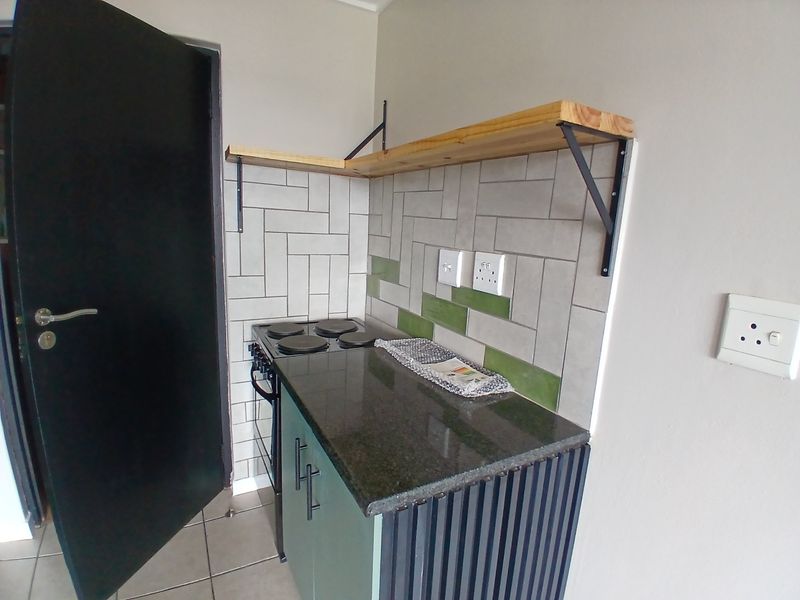 Compact kitchen area featuring a built-in electric stove, granite countertop, subway tile backsplash, and open wooden shelving.