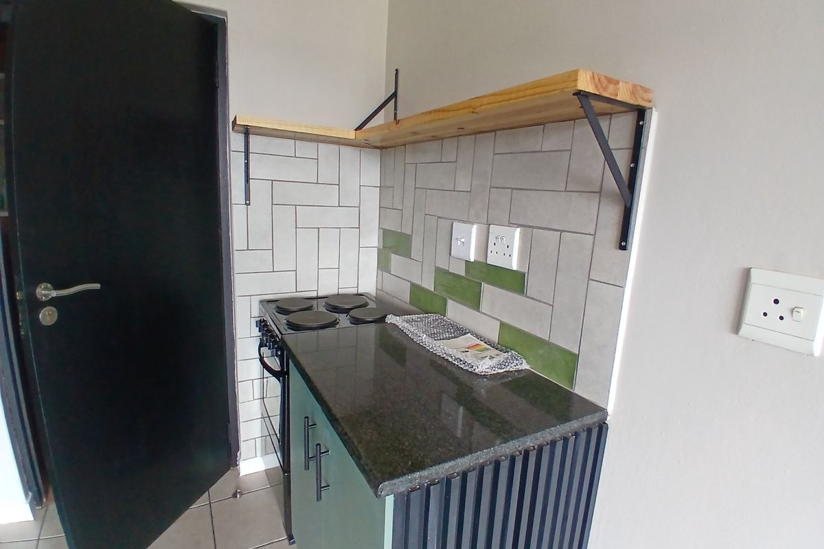 Compact kitchen area featuring a built-in electric stove, granite countertop, subway tile backsplash, and open wooden shelving.