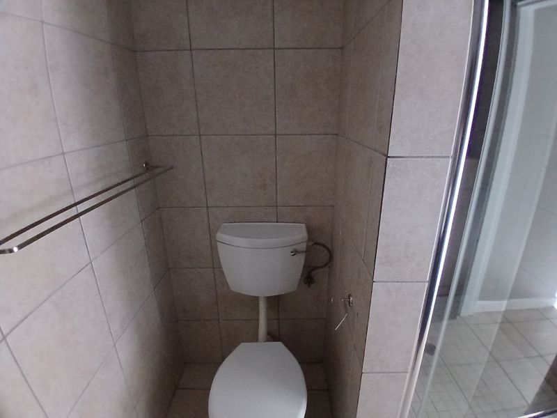 A functional bathroom featuring tiled walls and flooring, a standard toilet, and a glass shower enclosure.