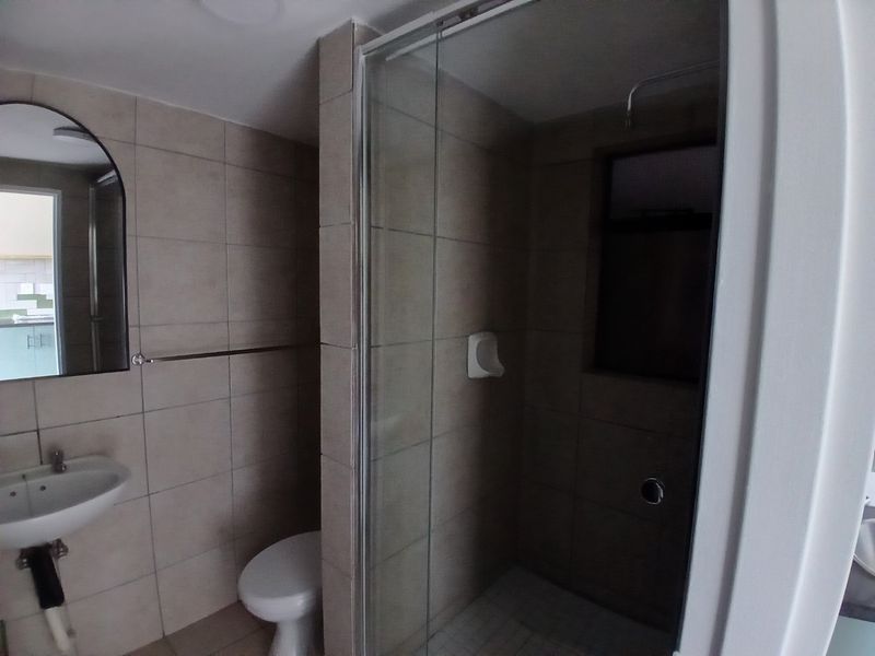 A functional bathroom featuring a pedestal basin, toilet, and a glass-enclosed shower with neutral wall and floor tiling.