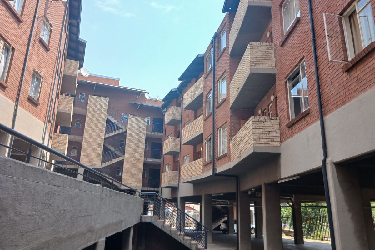 Exterior view of a multi-story apartment complex featuring face brick facades, concrete staircases, and integrated balcony structures with covered ground-level parking.
