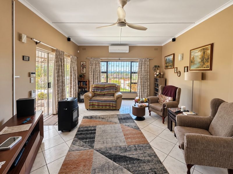 A comfortable living room featuring tiled flooring, a ceiling fan, split-system air conditioning, and large windows with security bars and sliding door access.