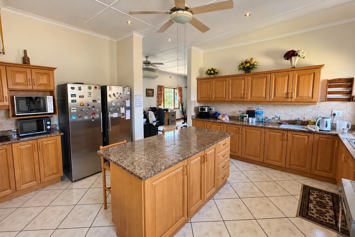 Spacious kitchen featuring wooden cabinetry, granite countertops, a central island, and tiled flooring, offering a functional layout with ample storage space.