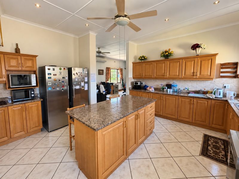 Spacious kitchen featuring wooden cabinetry, granite countertops, a central island, and tiled flooring, offering a functional layout with ample storage space.