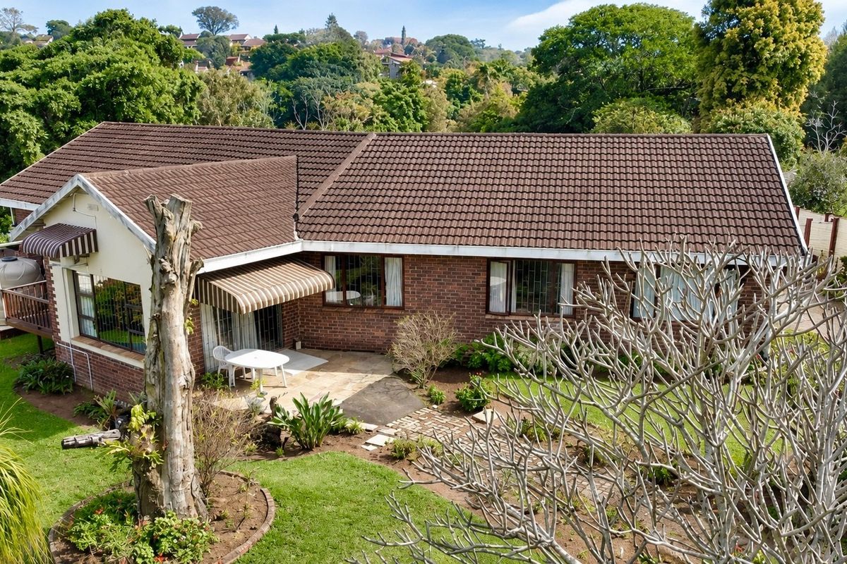 Aerial view of the rear of the brick house featuring a tiled roof, paved patio area, and established garden surroundings.