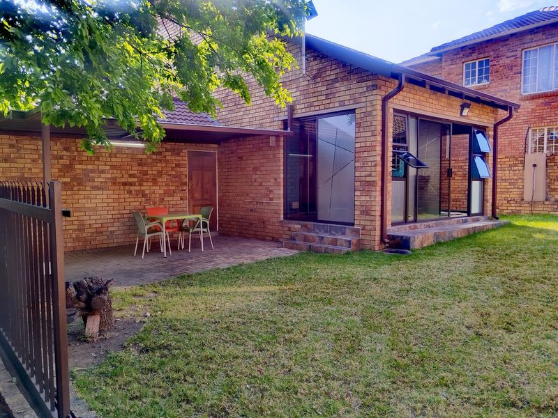 Rear view of a face brick townhouse featuring a covered patio, paved outdoor area, and a private lawn with large glass sliding doors.