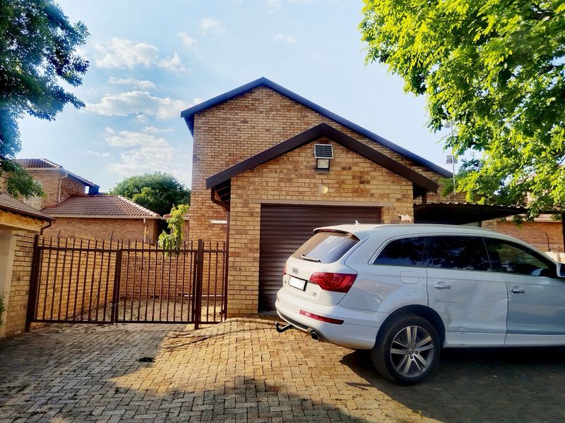 Front view of a brick townhouse featuring a paved driveway, secure metal gate, and a single garage.