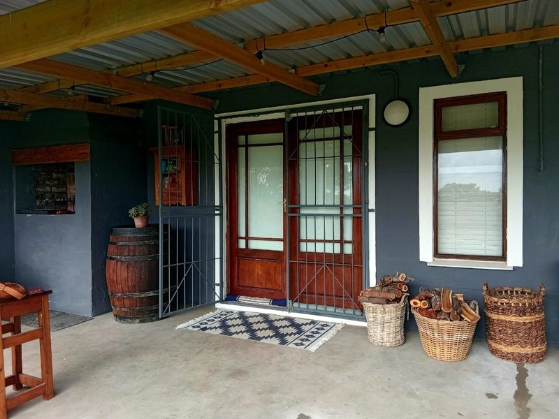 A covered patio area featuring a built-in braai, timber-framed glass doors with security gates, and a corrugated metal roof structure.