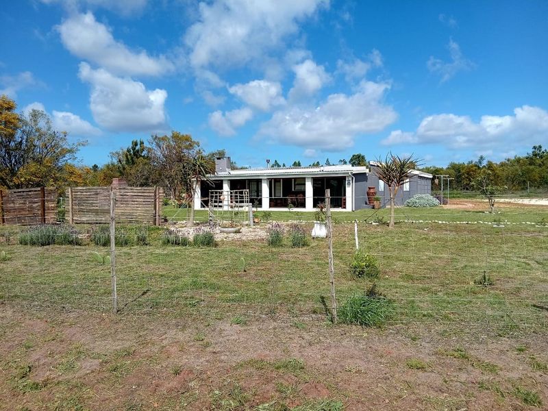 Rear view of the small holding property featuring a covered patio, external chimney, and expansive garden area enclosed by wire fencing.