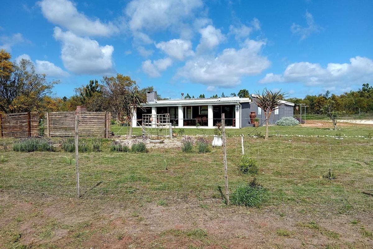 Rear view of the small holding property featuring a covered patio, external chimney, and expansive garden area enclosed by wire fencing.