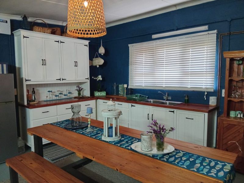 A rustic-style kitchen featuring white built-in cabinetry, wooden countertops, a double basin sink, and deep blue walls with venetian blinds.