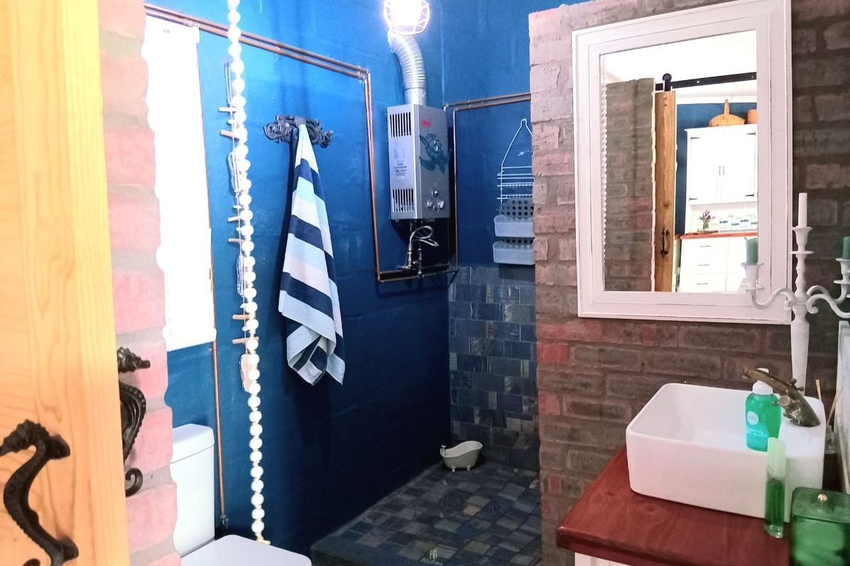 A rustic-style bathroom featuring exposed brick walls, a vessel sink on a wooden vanity, and a gas geyser unit.