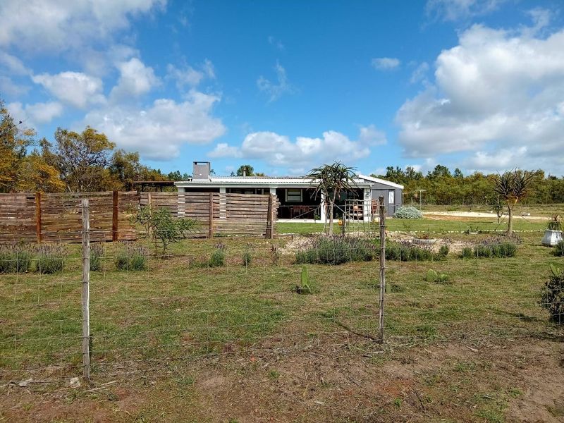 Rear view of the property featuring a covered patio, outdoor fireplace, and timber fencing set within a spacious garden landscape.