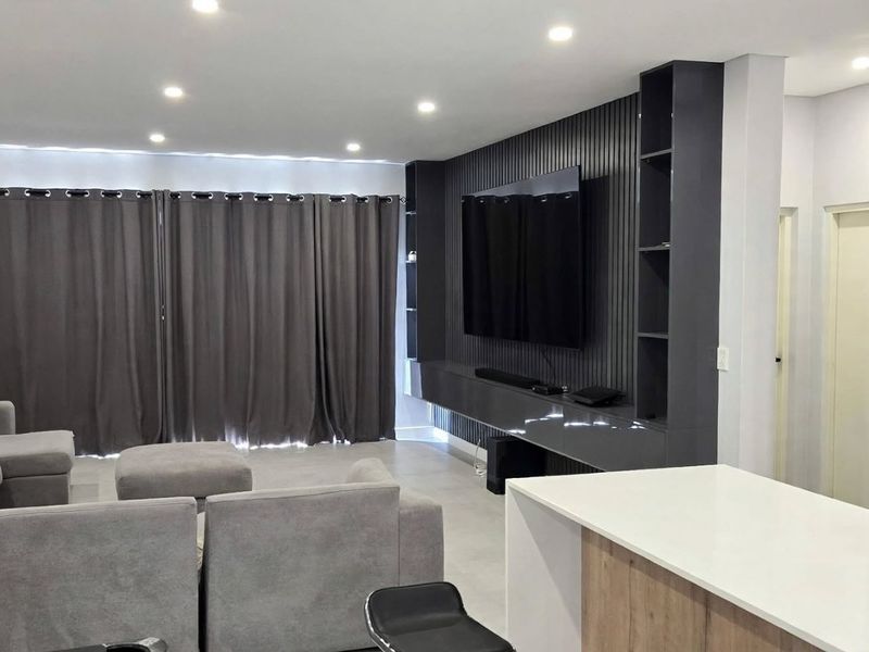 Modern open-plan living area featuring a sleek built-in media wall, recessed lighting, and a contemporary kitchen with integrated appliances.