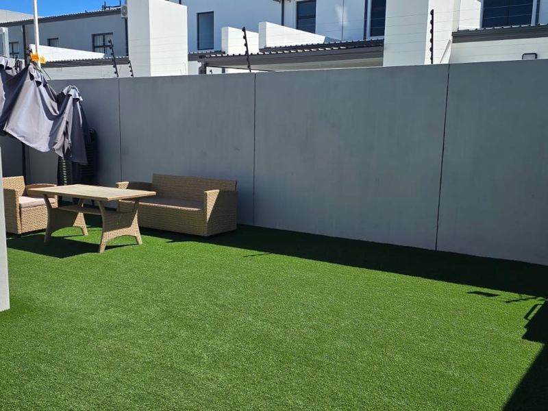A private rear courtyard featuring low-maintenance artificial turf, enclosed by high boundary walls with integrated electric security fencing.