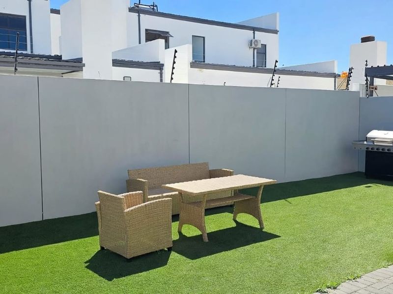 A private outdoor patio area featuring a built-in braai, artificial lawn, and secure perimeter walling with electric fencing.