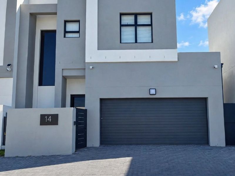 Modern double-storey residential facade featuring a sleek grey and white exterior, paved driveway, and integrated double garage.