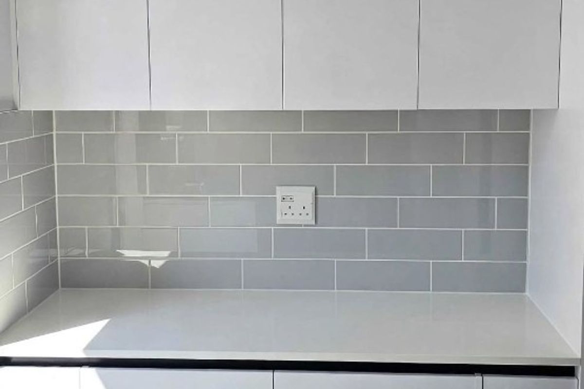 A clean, modern kitchen area featuring white cabinetry, a white quartz countertop, and a grey subway tile backsplash.