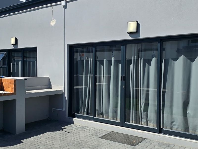 A modern paved patio area featuring a built-in brick braai and large sliding glass doors providing seamless access to the interior living space.