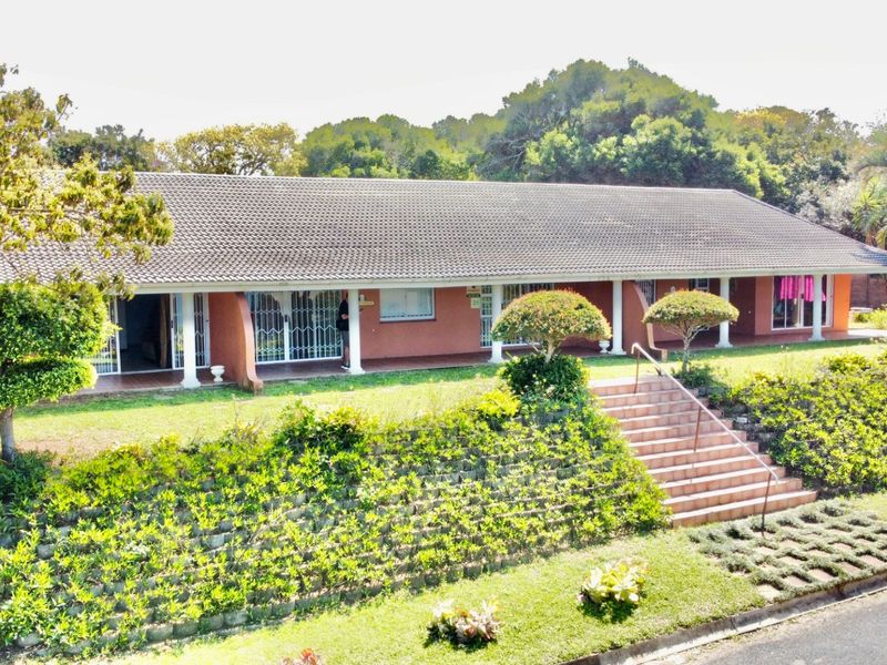 A single-story residential property featuring a long covered veranda, tiled roof, and a prominent brick staircase leading to a landscaped front garden.