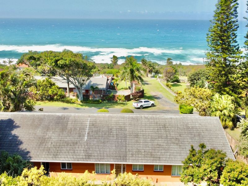 Aerial view of the property showcasing the tiled roof, surrounding garden, and proximity to the coastline.