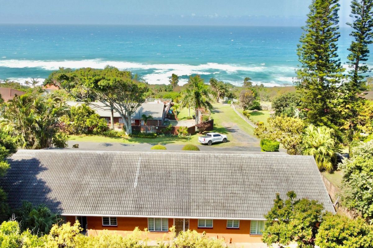 Aerial view of the property showcasing the tiled roof, surrounding garden, and proximity to the coastline.