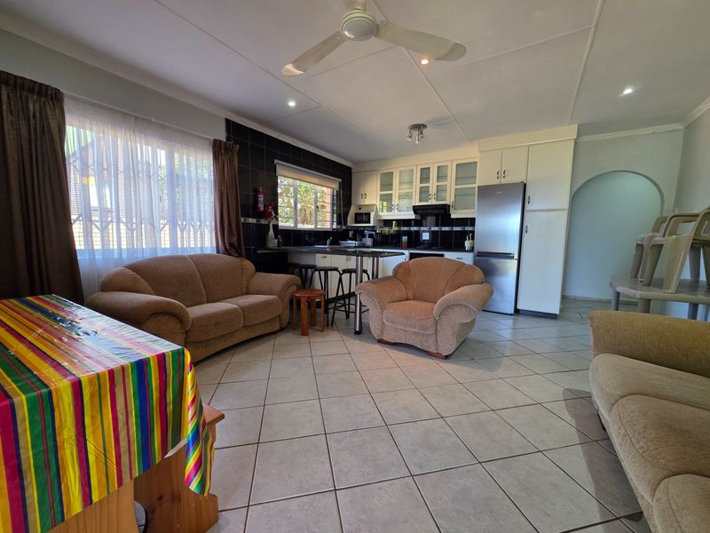 Open-plan living and kitchen area featuring tiled flooring, a ceiling fan, and a functional kitchen layout with built-in cabinetry and a breakfast bar.