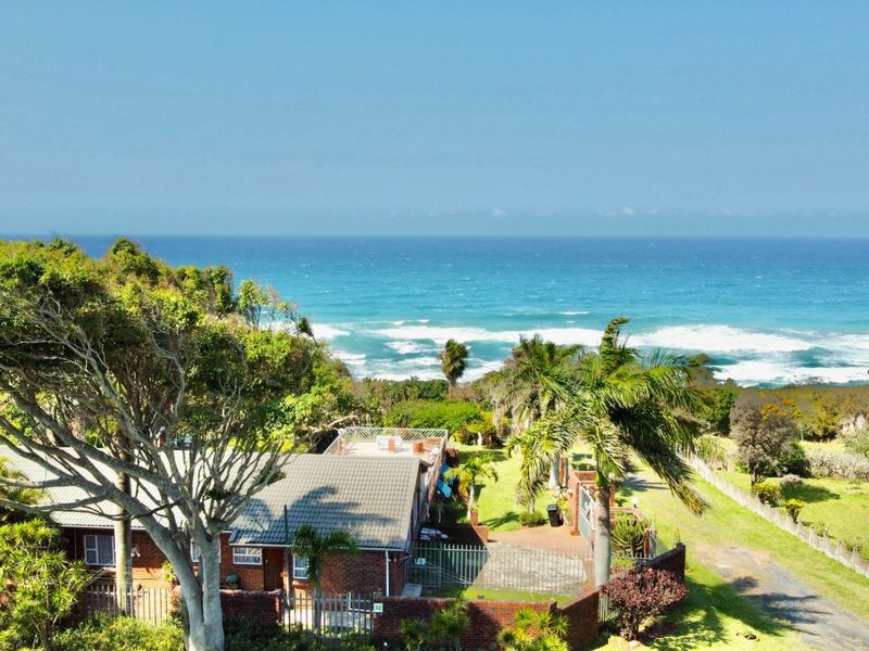 Aerial view of a coastal property featuring a brick house, established garden, and direct proximity to the ocean.