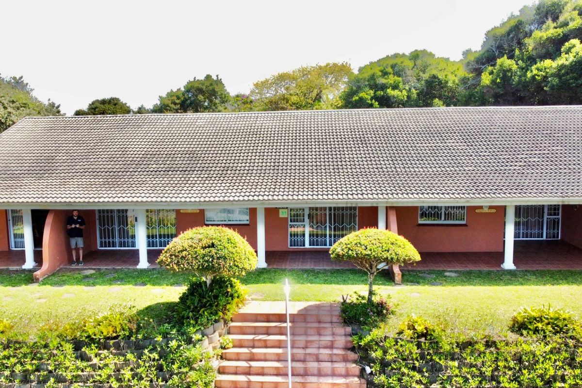 A rear view of the house featuring a long covered patio, tiled staircase, and established garden surroundings.