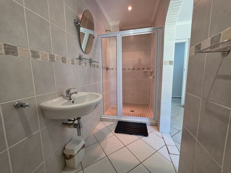 A functional bathroom featuring a wall-mounted basin, a tiled shower enclosure, and neutral wall and floor tiling.