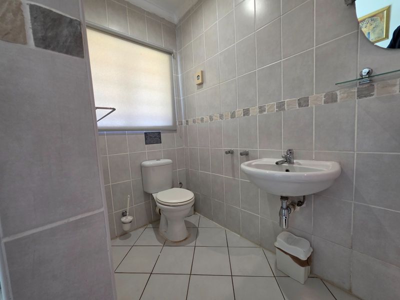 A functional bathroom featuring neutral ceramic wall and floor tiles, a wall-mounted basin with chrome fixtures, and a standard toilet.