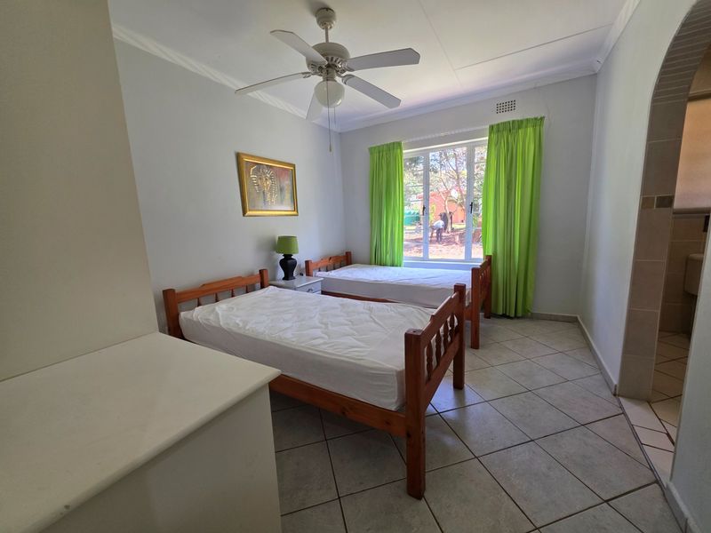 A functional bedroom featuring tiled flooring, a ceiling fan, and a built-in cupboard, with natural light provided by a large window.