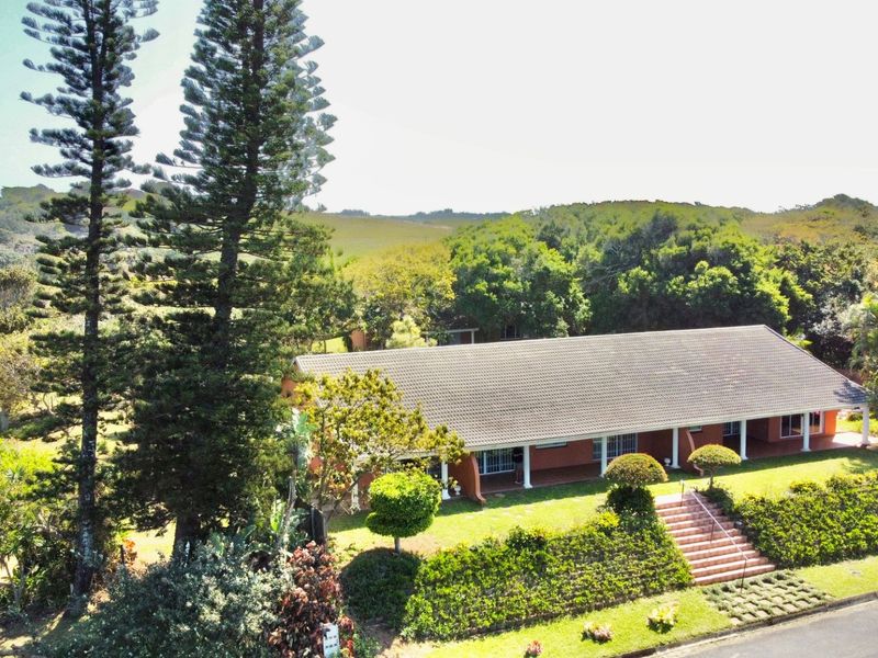 Aerial view of a single-story brick residence featuring a tiled roof, a spacious covered patio, and well-maintained landscaped gardens.