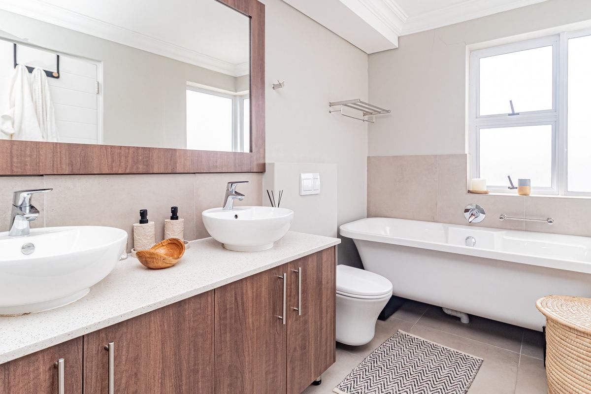 Modern bathroom featuring a double vanity with vessel sinks, a freestanding bathtub, and neutral tiling, offering a clean and contemporary aesthetic.