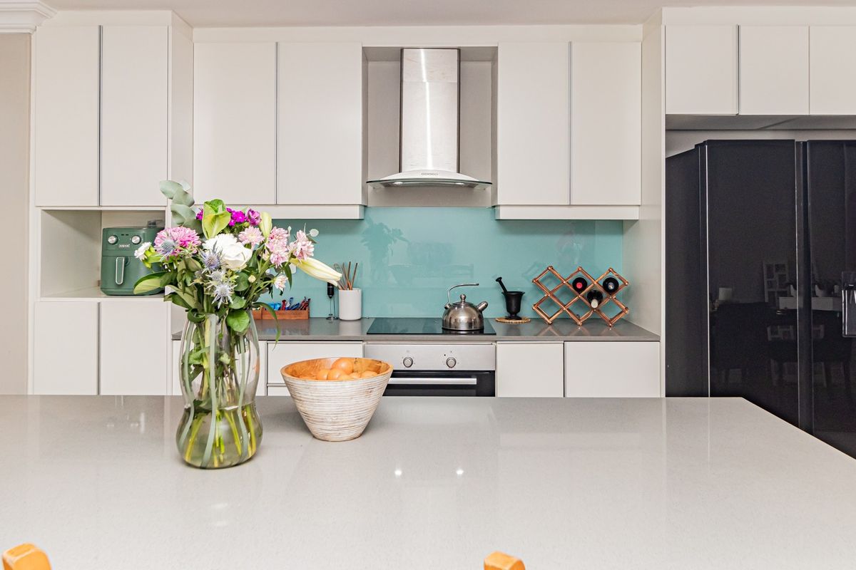 Modern kitchen featuring sleek white cabinetry, stone countertops, a glass splashback, and a central island, complemented by integrated appliances.