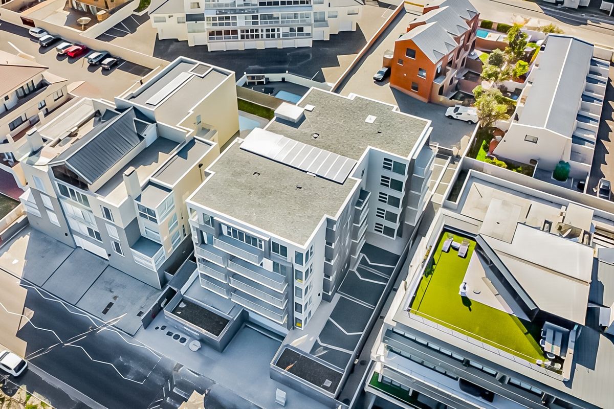 Aerial view of the apartment complex showing the building structure, roof-mounted solar panels, and surrounding urban layout.