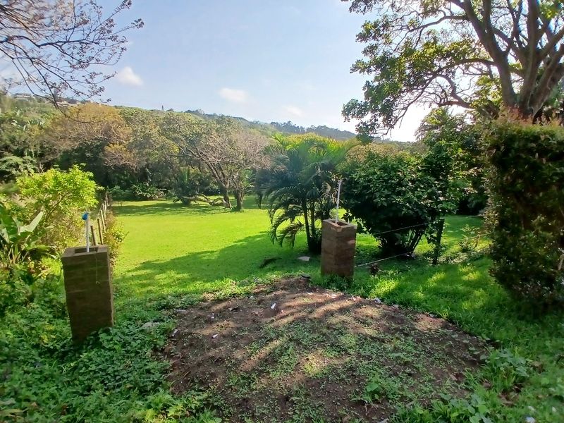 A view of a spacious, green residential garden featuring mature trees and brick gate pillars, offering a natural and tranquil outdoor setting.