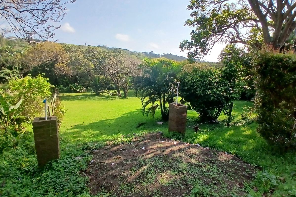 A view of a spacious, green residential garden featuring mature trees and brick gate pillars, offering a natural and tranquil outdoor setting.