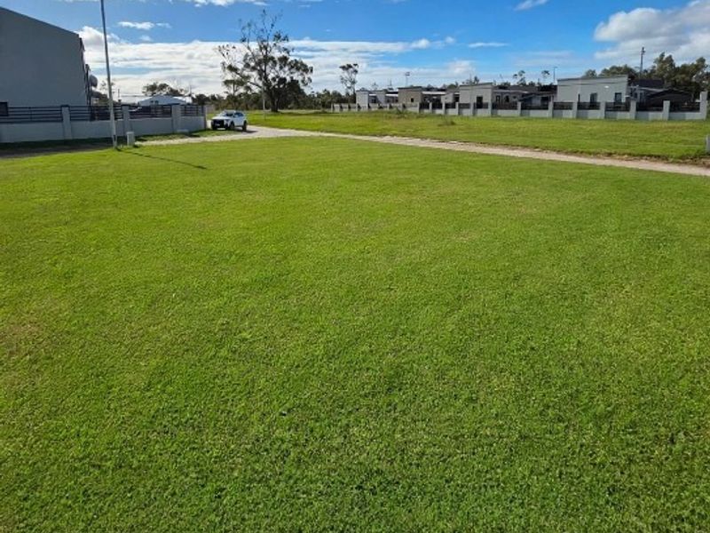 A spacious, well-maintained vacant residential plot featuring a level grass lawn and established boundary fencing in a quiet neighborhood setting.