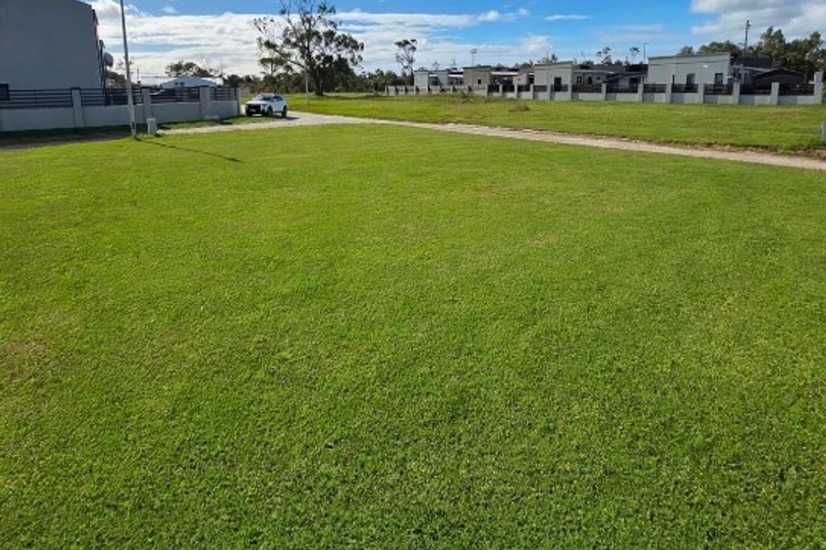 A spacious, well-maintained vacant residential plot featuring a level grass lawn and established boundary fencing in a quiet neighborhood setting.