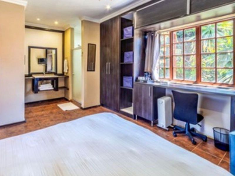 Spacious bedroom featuring built-in cupboards, a dedicated desk area, tiled flooring, and an en-suite vanity with a mirror.