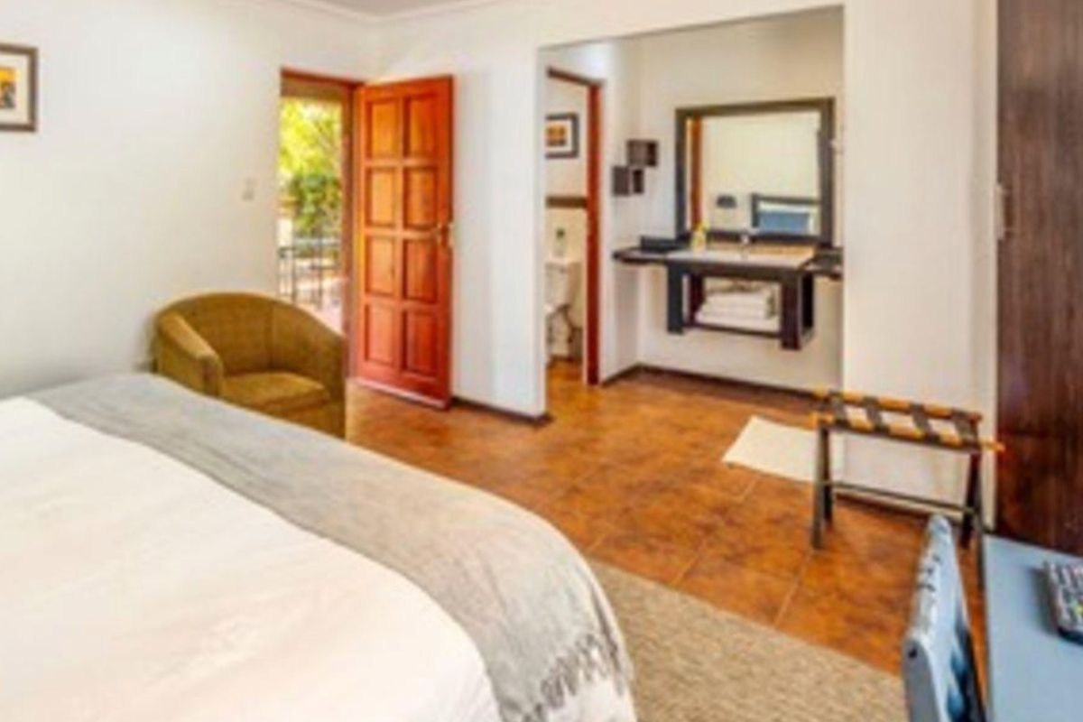 A bedroom featuring tiled flooring, an en-suite bathroom with a built-in vanity, and direct access to an outdoor area through a wooden door.
