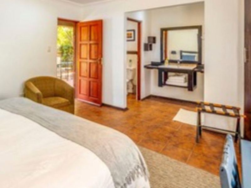 A bedroom featuring tiled flooring, an en-suite bathroom with a built-in vanity, and direct access to an outdoor area through a wooden door.