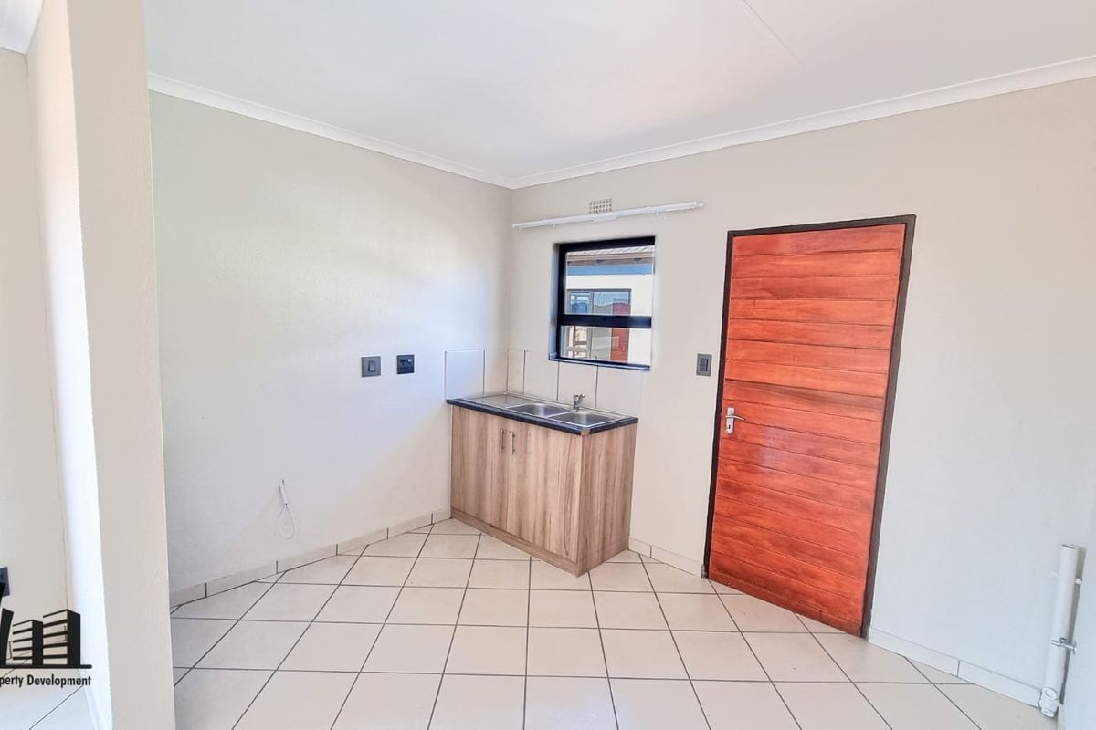 A clean, compact kitchen area featuring tiled flooring, a single base cabinet with a sink, and a solid timber door.